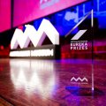 A photo of a stage, lit up with pink and blue lights, and a glass trophy in the foreground saying Eureka Prizes.